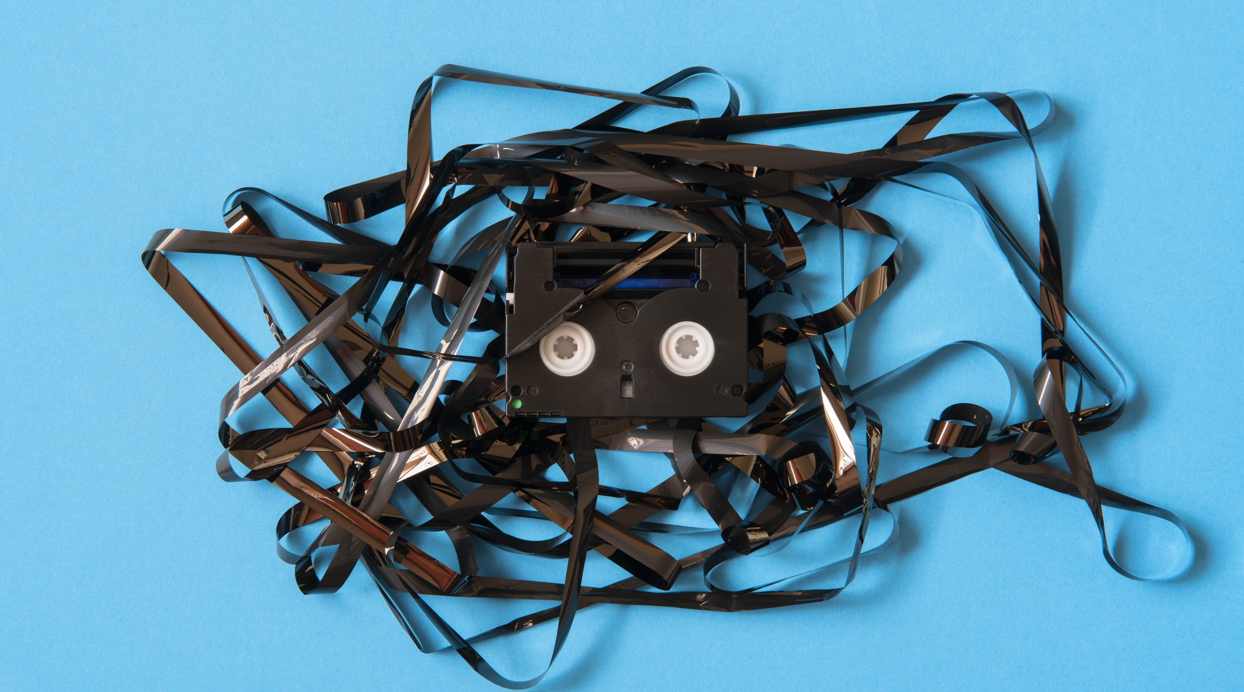 cassette tape that was tangled around the casing in a chaotic manner on a solid blue background